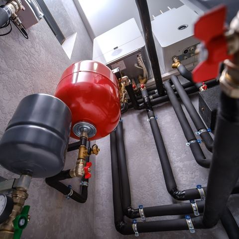 A boiler-room wall carrying expansion vessels, a pressure gauge and insulated flow and return pipework
