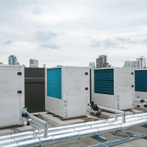 Packaged commercial condensing units lined up on a roof deck against a city skyline