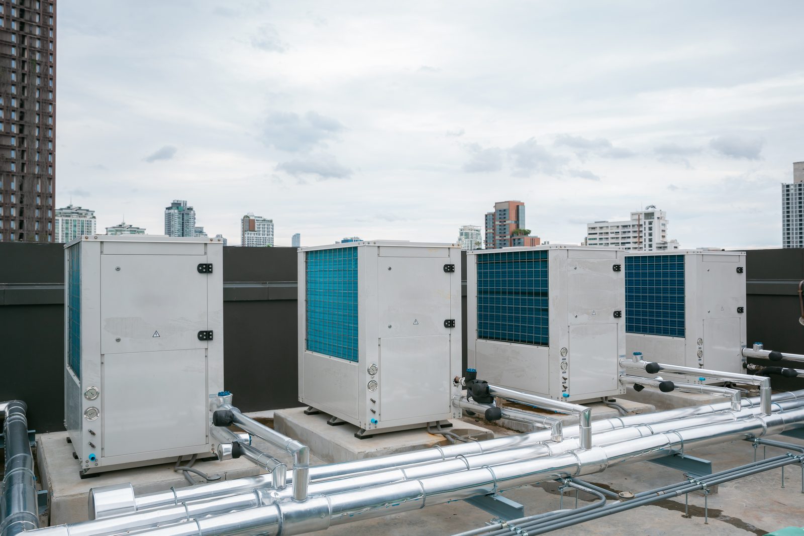 A bank of packaged rooftop condensing units on a city roof deck, with insulated pipework running in the foreground