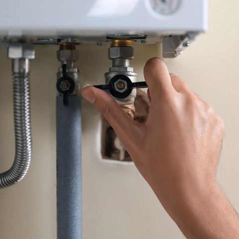 A hand closing an isolation valve on the pipework beneath a wall-hung tankless water heater