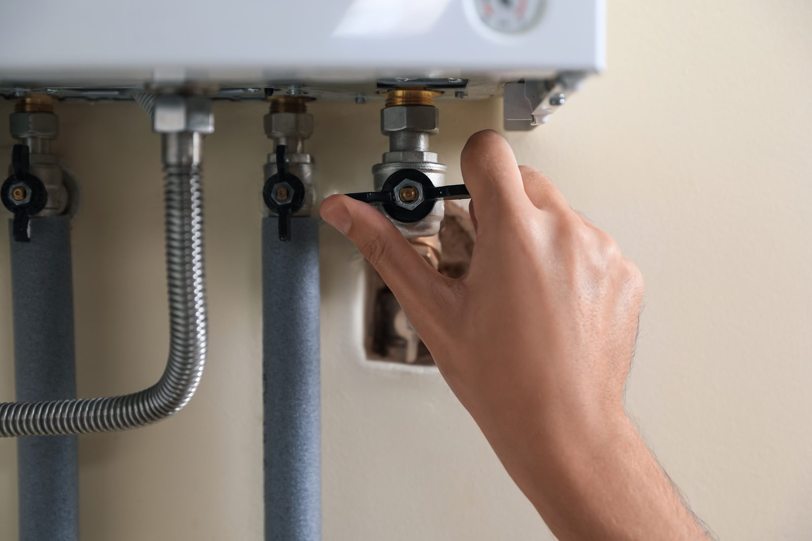 A hand closing an isolation valve on the pipework beneath a wall-hung tankless water heater